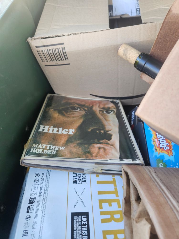 A hardback book titled "Hitler" in a bin full of cardboard boxes and empty wine bottles 