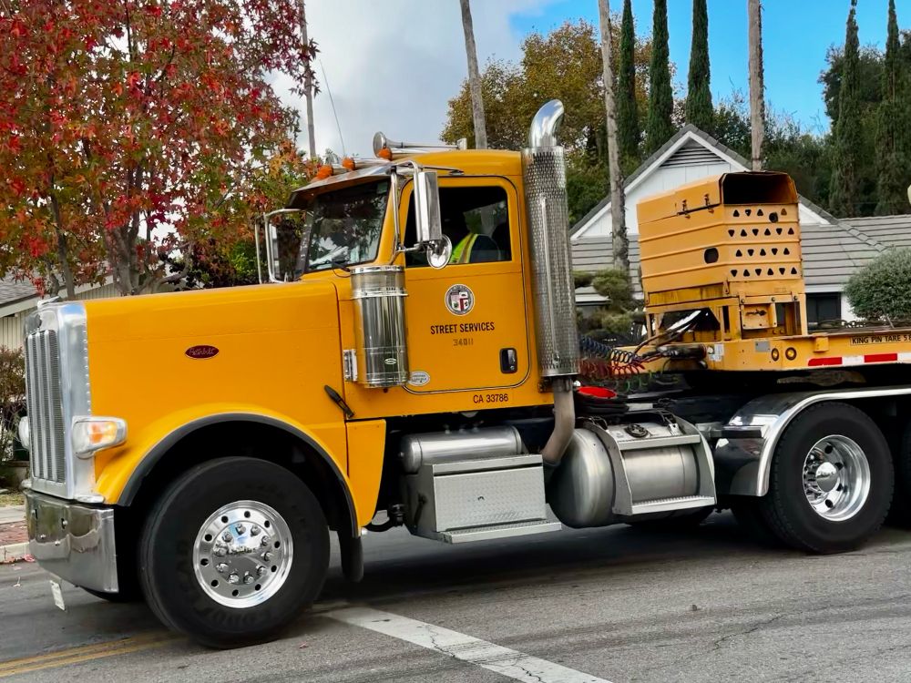 The front of a long yellow flatbed truck, part of the bed is visible. 