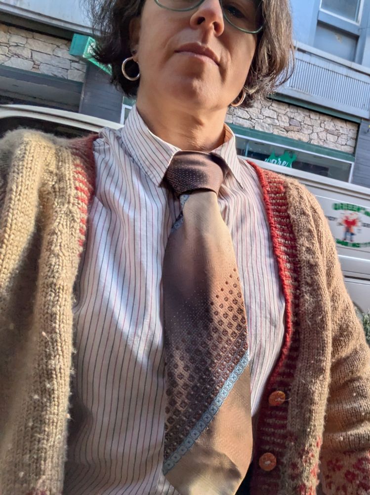 A woman wears a wide brown tie with a bright blue diagonal stripe and then stripes made of faded boxes. The other direction has a satin stripe too. 