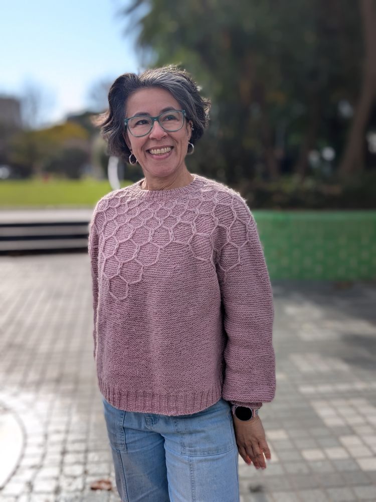 A woman stands outside wearing a pale pink jumper.
