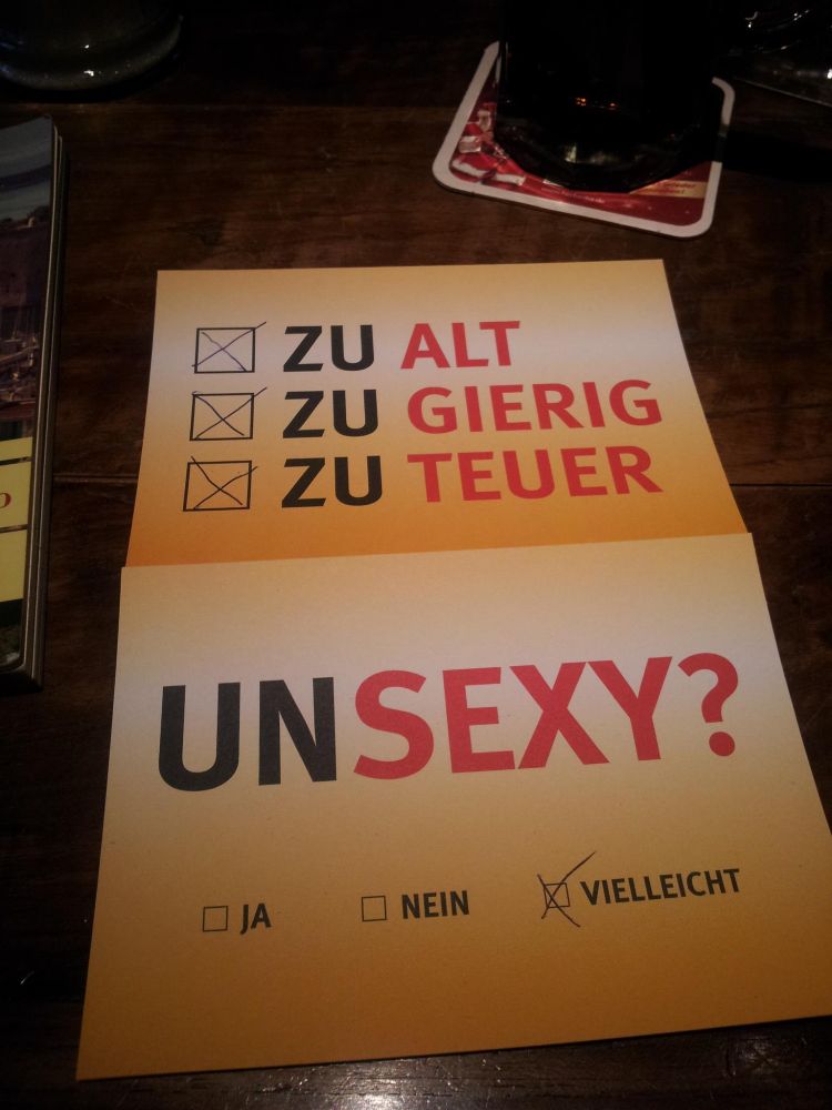 Zwei Postkarten mit Text. Auf der oberen sind drei Ankreuzkästchen mit den Beschriftungen "zu alt", "zu gierig", "zu teuer" und alle drei sind angekreuzt. Auf der unteren Karte steht "Unsexy?" mit den Auswahlmöglichkeiten "Ja", "Nein", "Vielleicht". Letzteres ist angekreuzt.