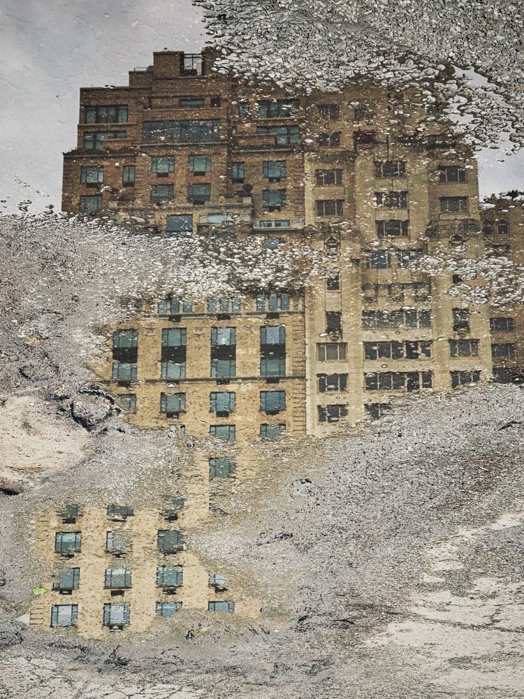 Image of a puddle reflection of a New York City building on a path in Central Park South, NYC, USA.