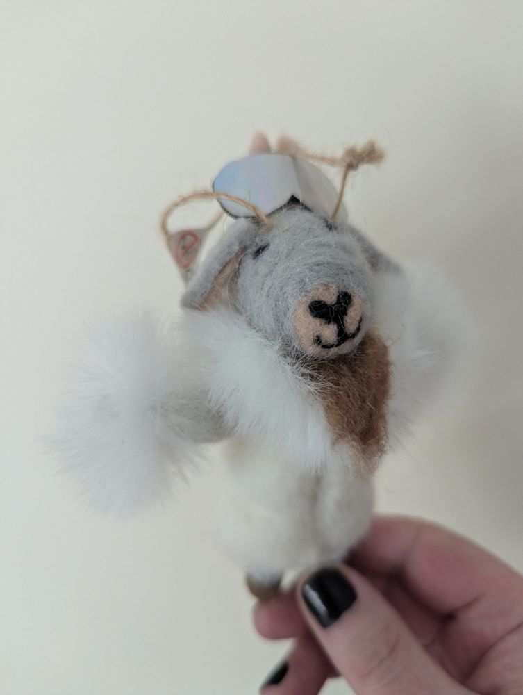 A felt christmas tree decoration, shaped like a goat wearing a fur coat, with mirrored sunglasses