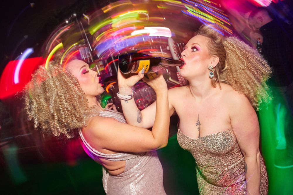 Two Glamorous ladies with big hair drink from bottles of fizz 