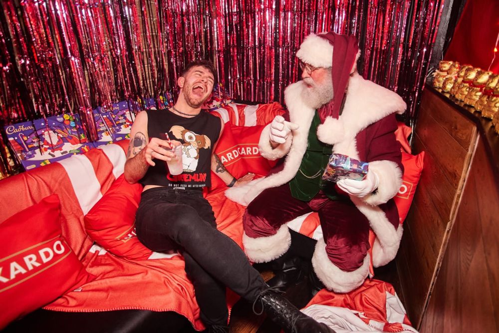 A young man in Gremlins T-shirt laughs with Santa Claus