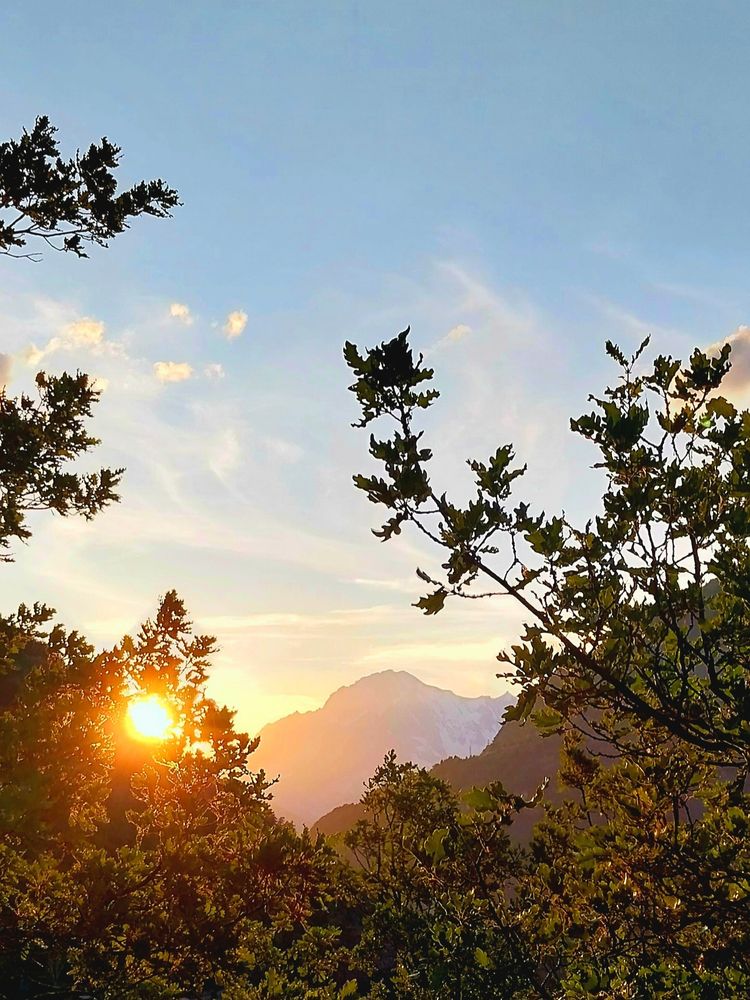 On the left, the sun setting between the oak branches in the Verney forest. At the center, a mountain and some clouds bathed in orange rays. 