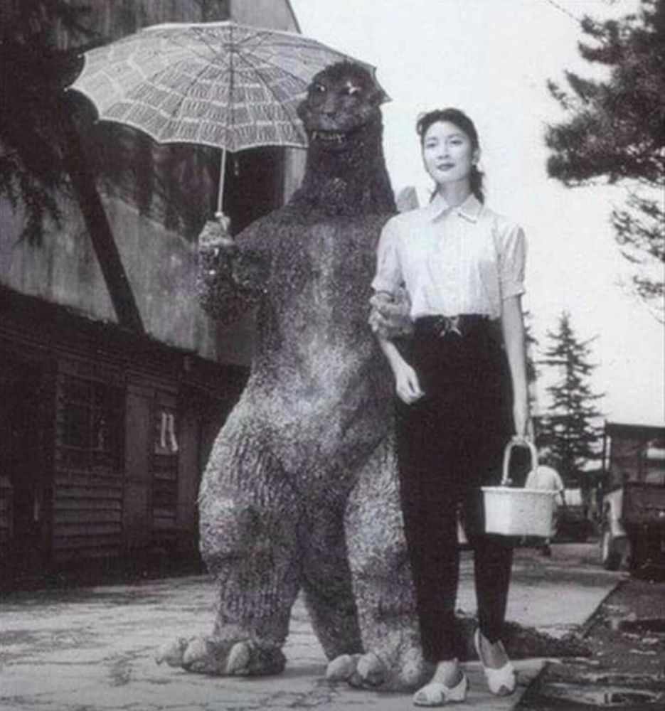 Old photo of Godzilla walking along a street with a woman, holding a parasol 