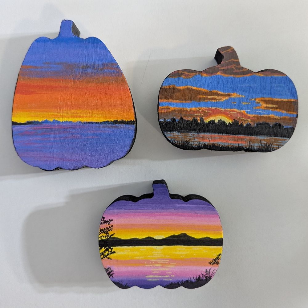 Three mini wooden pumpkins with different sunrise/sunsets painted on them.