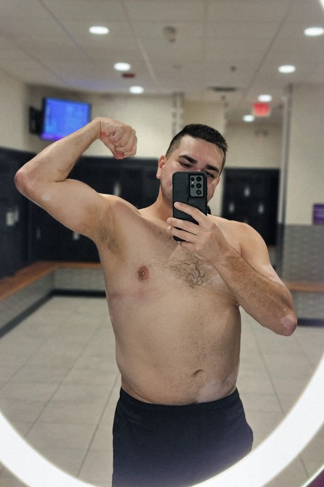 Locker room mirror selfie of me flexing with my shirt off post arms and chest day