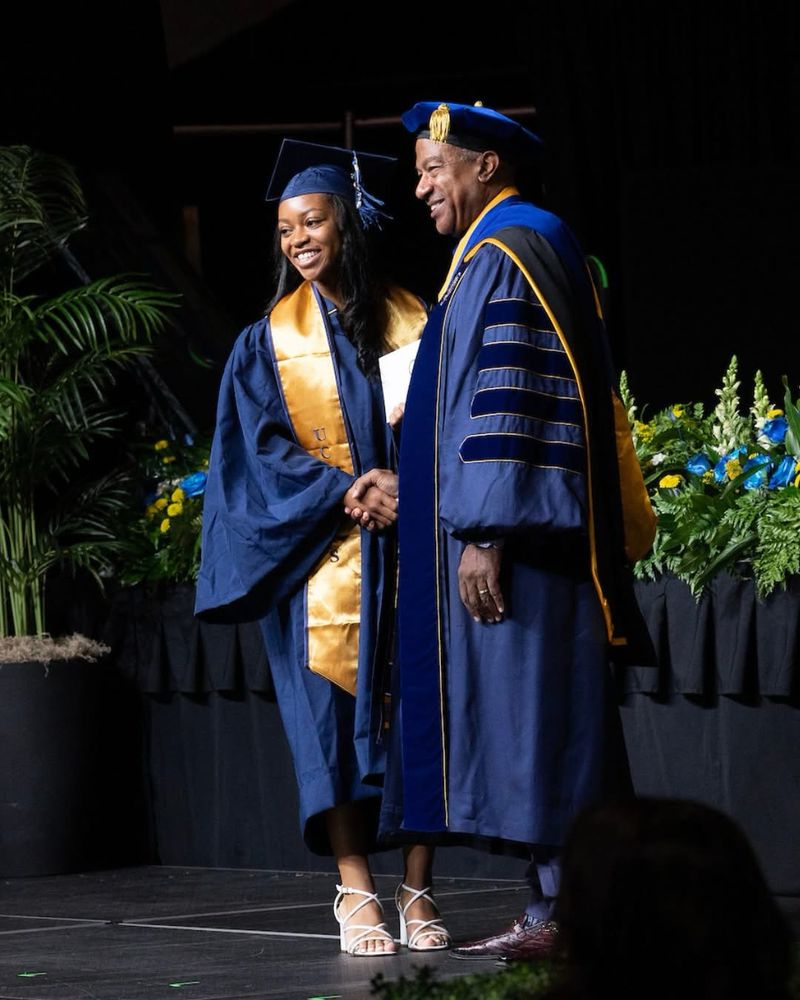 A graduate shakes hands with Chancellor May on stage and smile.