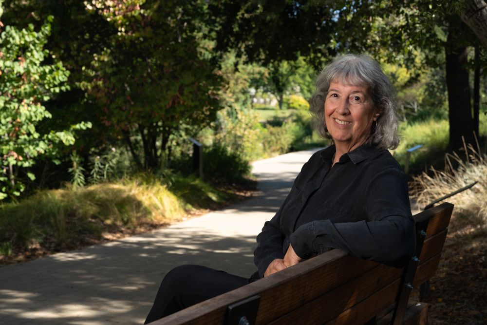 Kate Scow sits on a bench and leans back as she smiles a the camera.