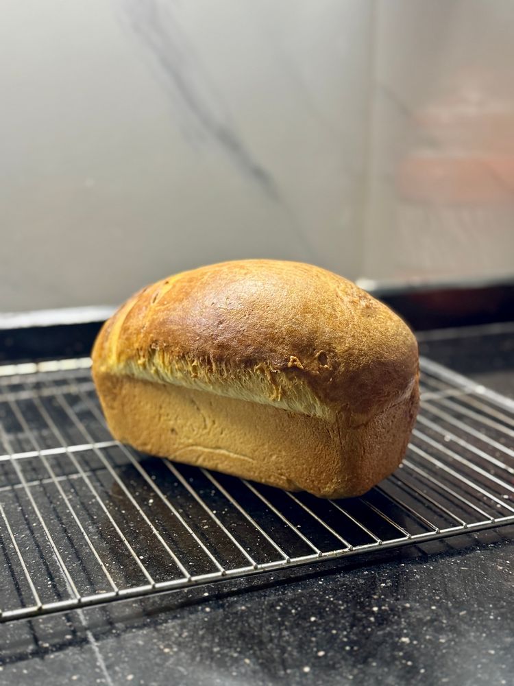 Picture of a brownish milk sandwich bread loaf resting on a cooling rack in my kitchen
