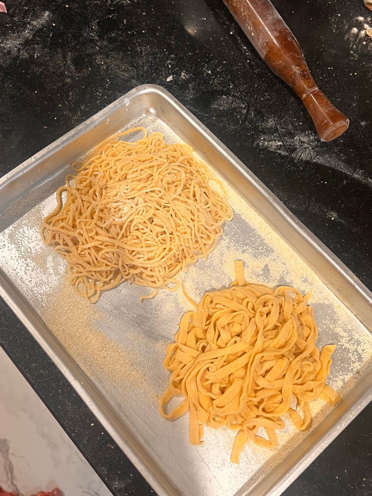A sheet pan with a pile of yellow spaghetti and a pile of yellow fettuccine, freshly made and drying out on the open