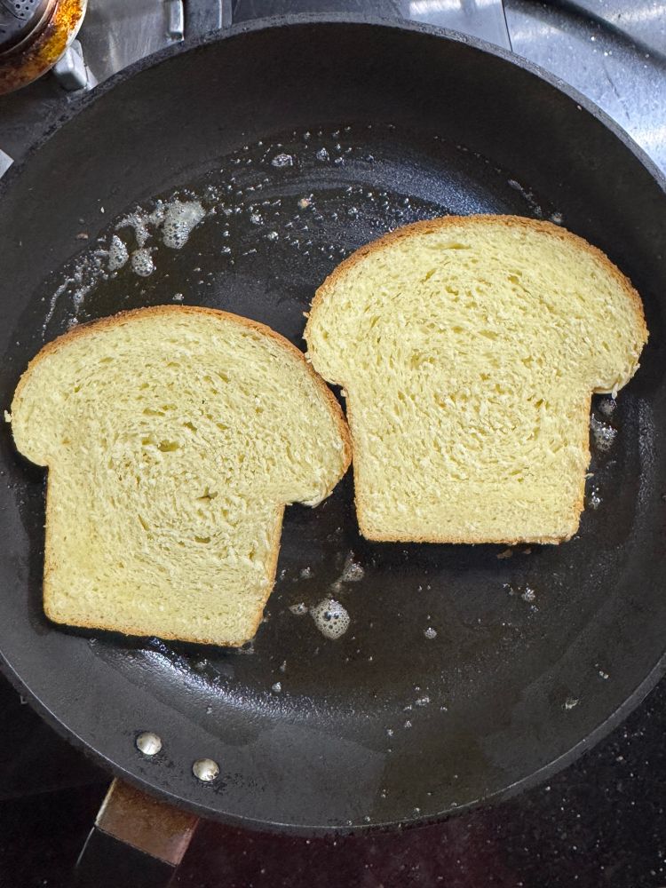 2 slices of milk sandwich bread toasting on a non stick pan with a little butter. 
