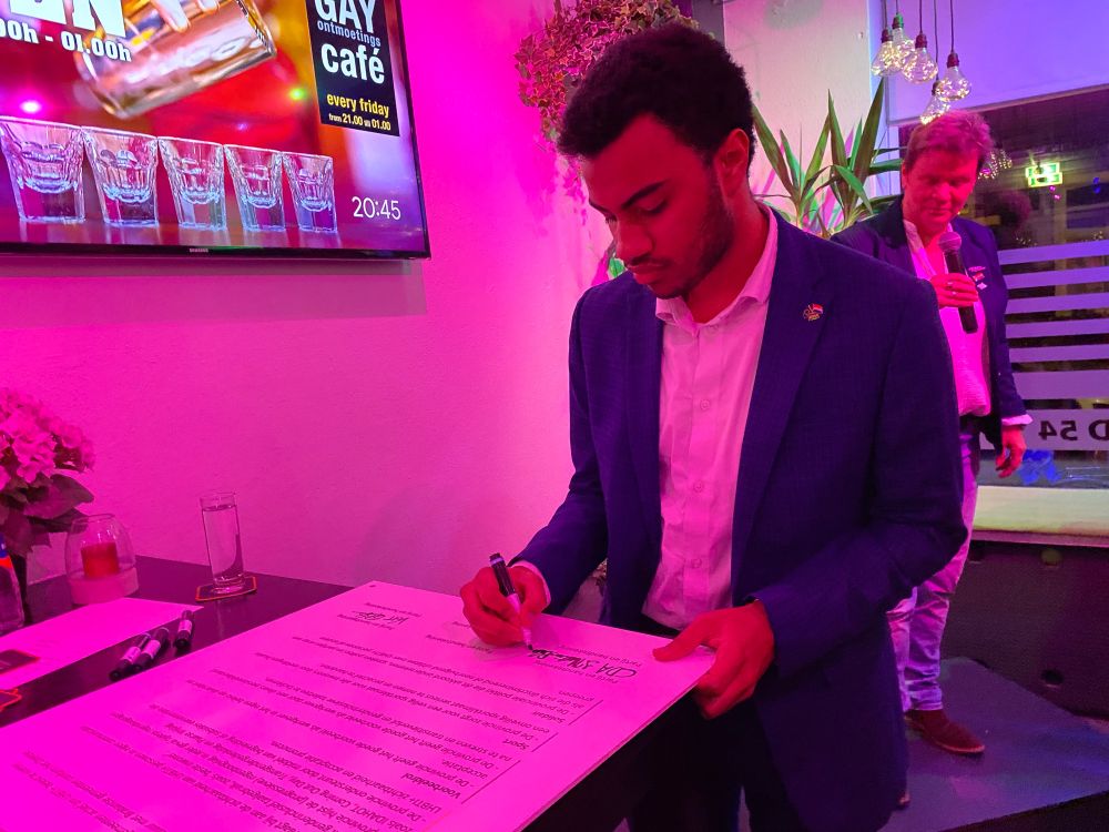 Ik onderteken het COC-Regenboogstembusakkoord. Ik draag een donkerblauw tweedelig pak met ruitjes en een wit overhemd. Ook draag ik op mijn pak mijn CDA-NL-EU-pin.