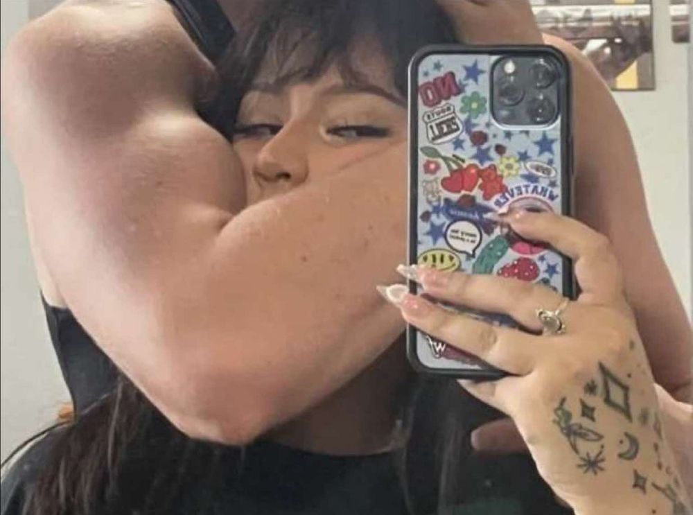 a happy woman has a arm wrapped around her head and is taking a mirror selfie