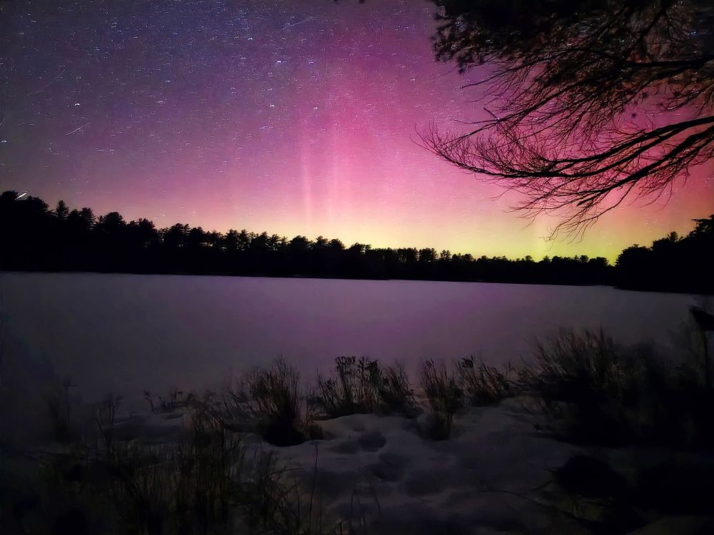 Pink and yellow Northern lights over a frozen lake.