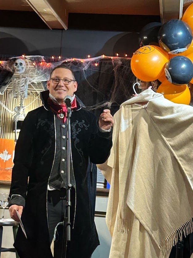 Avi auctioning off a fundraising serape in a vertical photo.