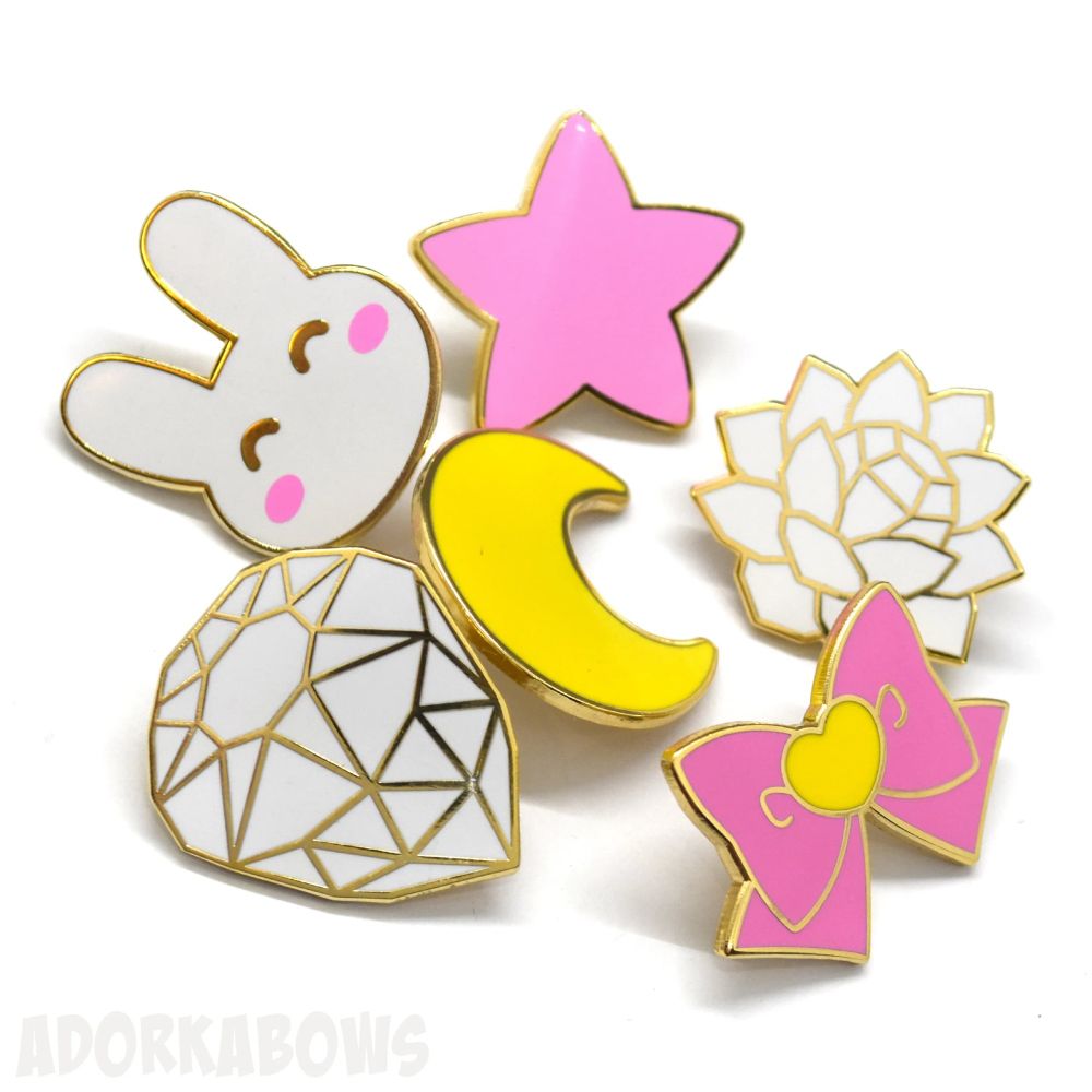 Six various shape and color enamel pins including a small happy bunny, a crystal, and a bow.