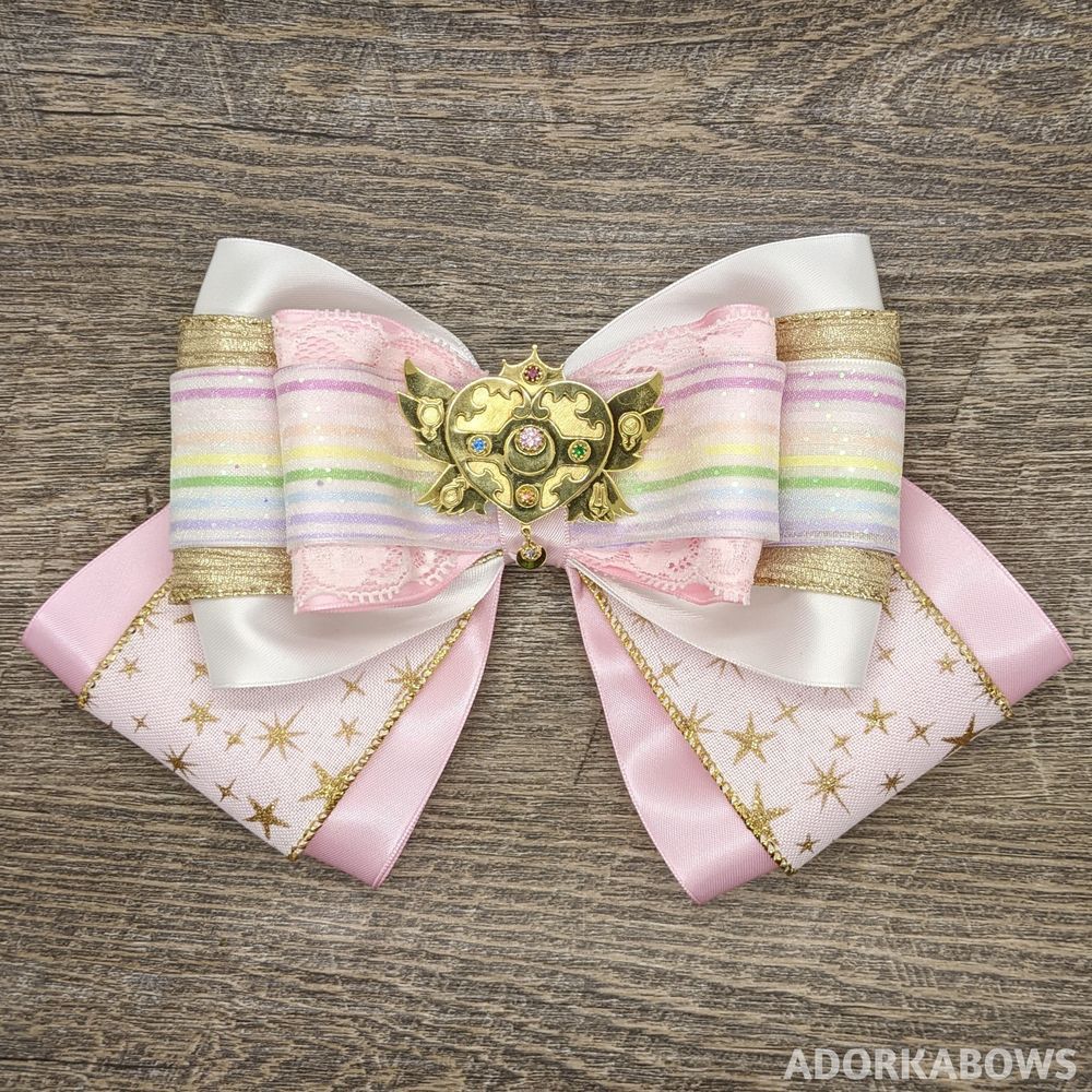 Light pink, white, gold, and rainbow bow with a golden Sailor Moon brooch in the center.