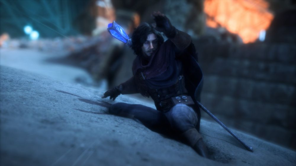 A digital photograph from Dragon Age The Veilguard. It shows the subject, a white older man with medium-length greyish brown curly hair with a mustache and goatee. He is in worn adventurers clothes with a staff stored on his back. He slides down a sandy slope.