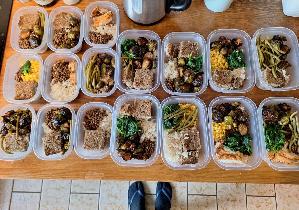 Foto de uma bancada de cozinha com 17 potinhos de marmita e na frente um par de pés com meia calçando chinelo 