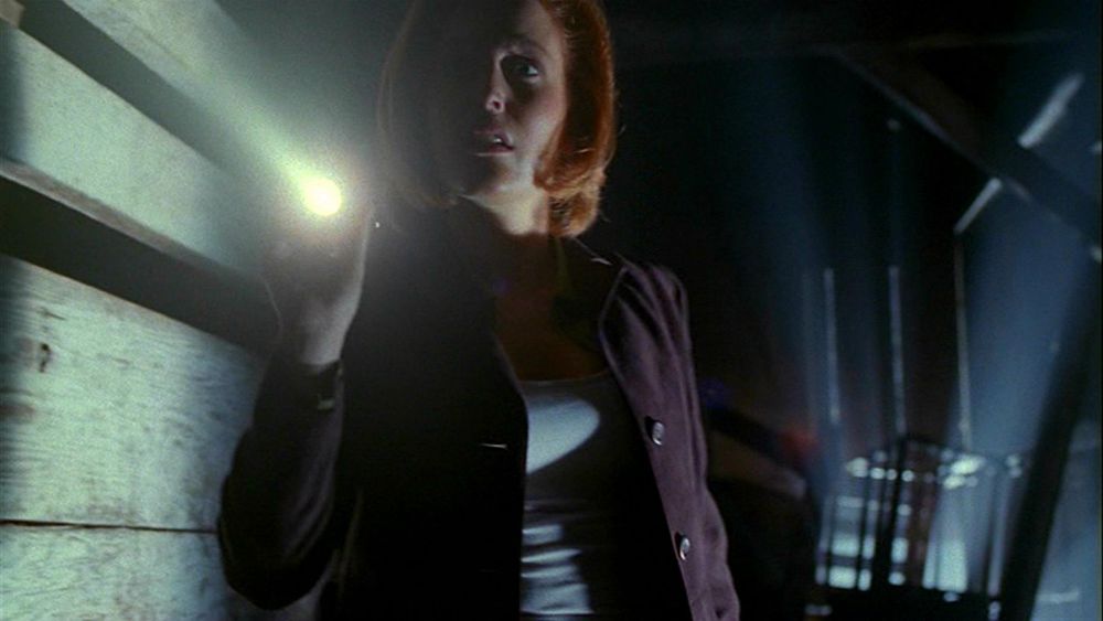 Dana Scully in the dark holding a LED torch.