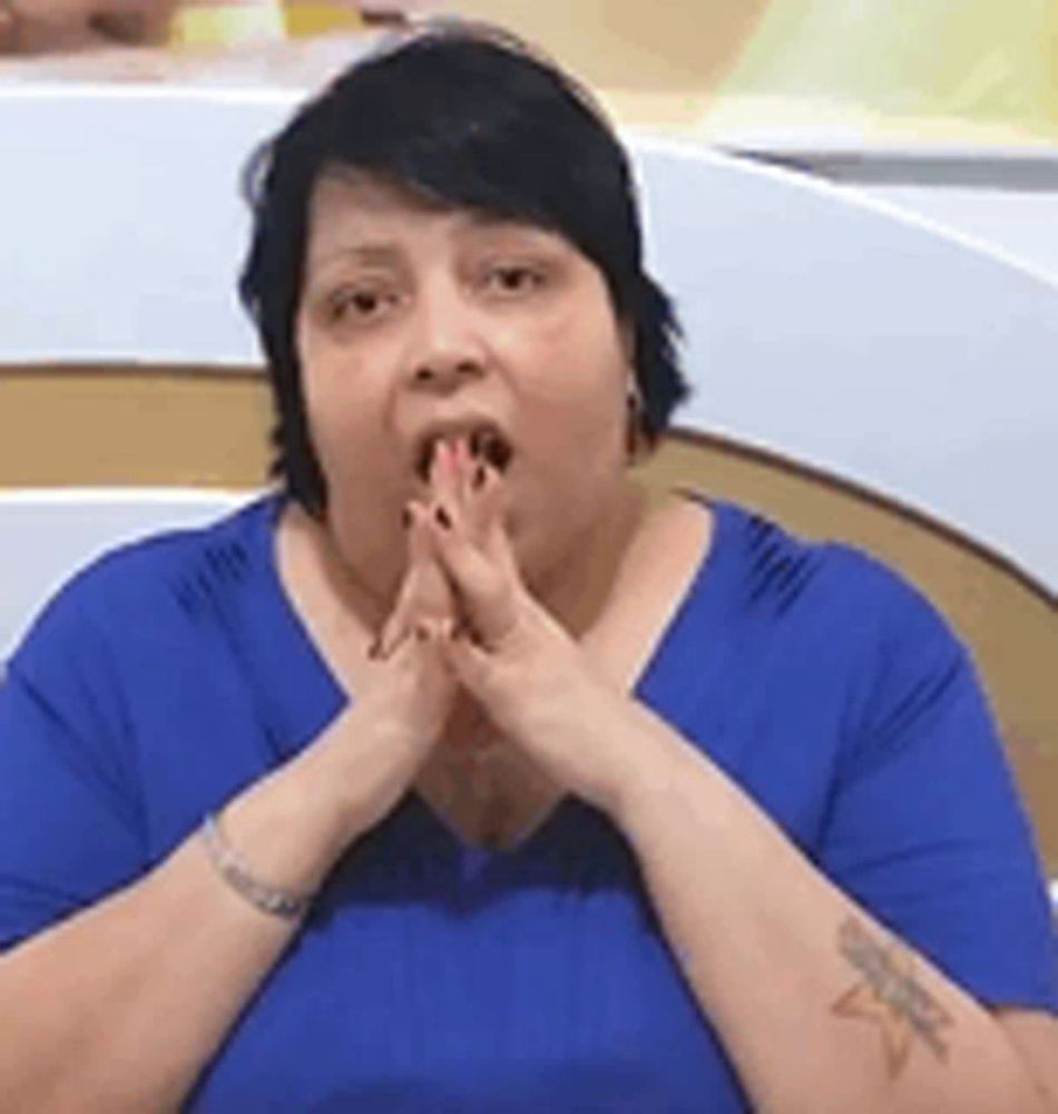 a woman in a blue shirt is covering her mouth with her hands and making a surprised face .