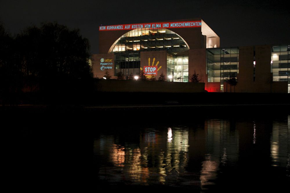 Foto von einem Gebäude, auf das etwas projiziert wurde. Eine gelbe Hand, auf der in einem roten Kasten STOP Mercosur steht. Darüber ist ein rotummantelter Text: Kein Kuhhandel auf Kosten von Klima und Menschenrechten.