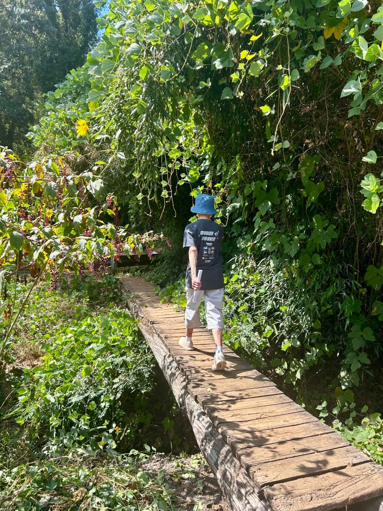 Woman facing away from camera walks across small wooden bridge in the woods