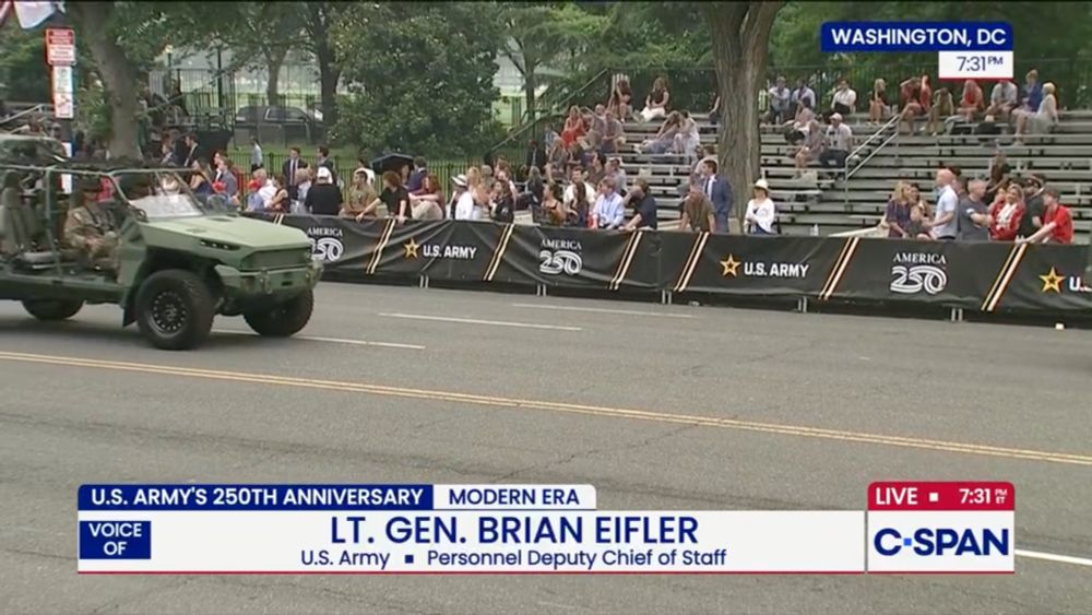 It shows a jeep driving through the parade, next to stands that are 25% full at most