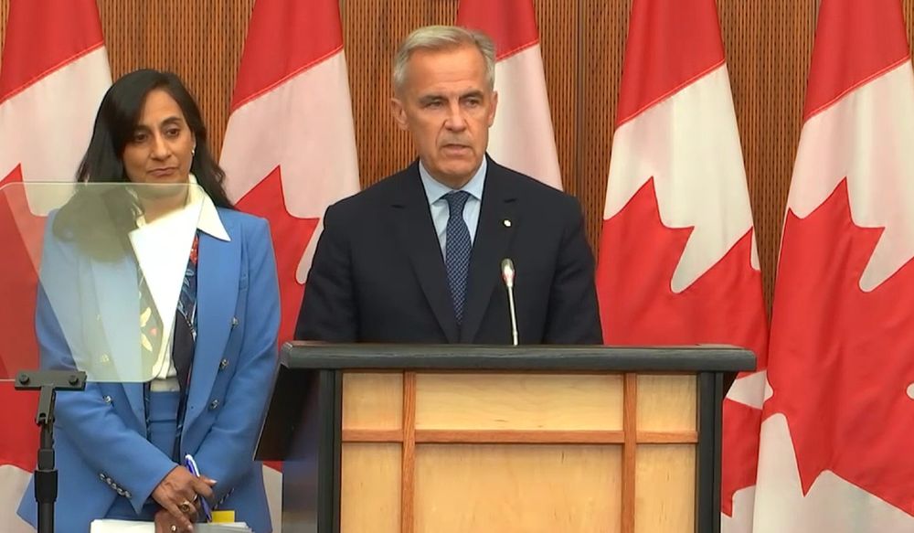 Mark Carney at a podium, flanked by Canadian flags. Behind him is Foreign Affairs Minister Anita Anand