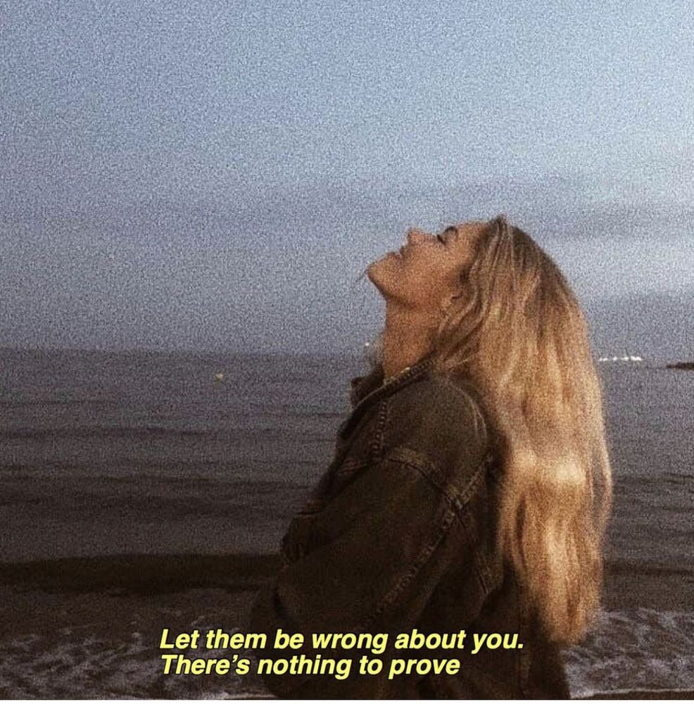 blonde girl smiling by the ocean with a caption on the phone that says “let them be wrong about you. there’s nothing to prove.”