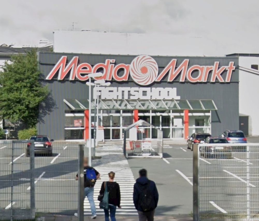 Google-Streetview Ausschnitt eines Parkplatzes mit dahinterliegenden Gebäude auf dem Media Markt Fight school steht. 