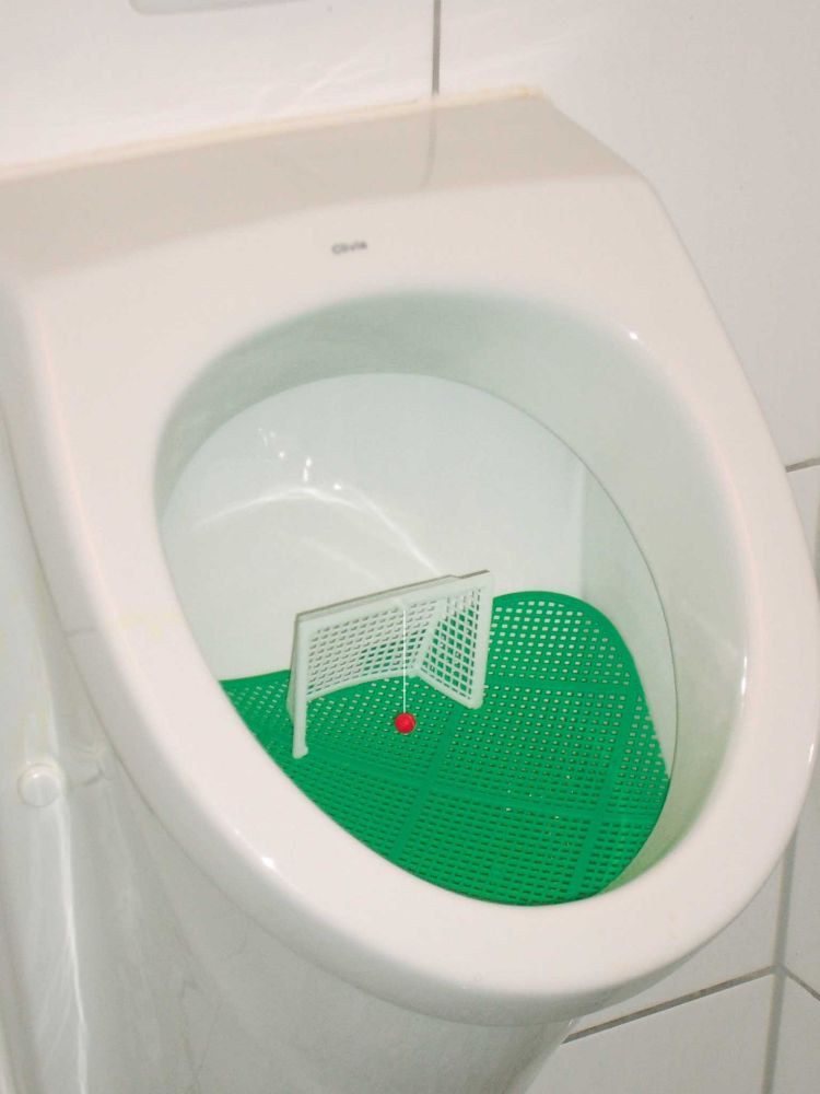 Fußballtor in einem Pissoir mit rotem Ball auf grüner Plastikfläche um das daneben pinkeln zu verhindern. 
