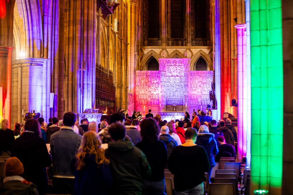 Truro cathedral lit up in rainbow colours and fill of people.