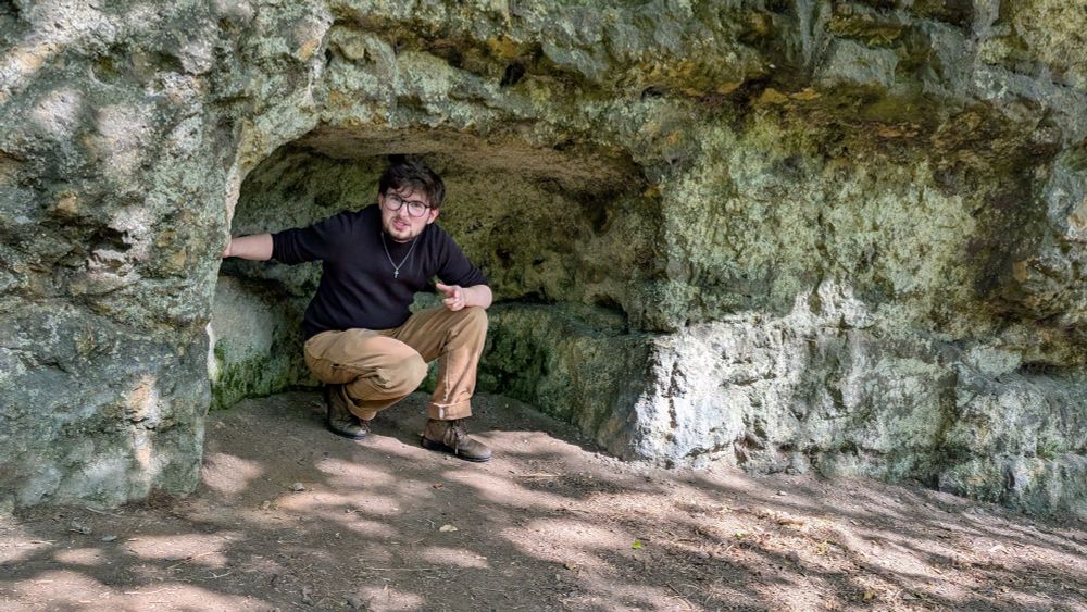 Jay squats in a small rock niche, he's mid-speech, his face kind of urgent and his hands gesturing 
