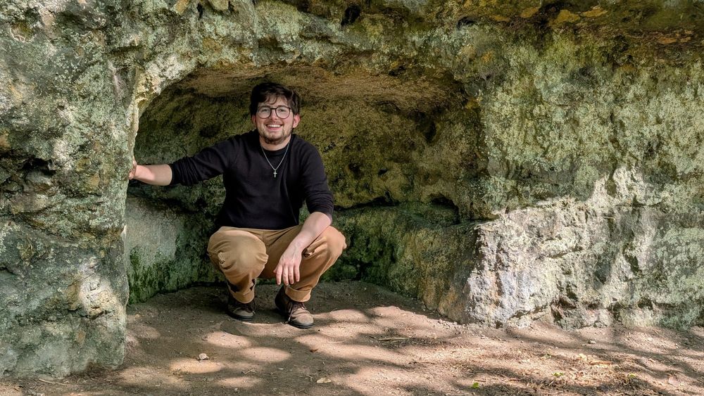 Jay squats in a small rock niche, he's smiling at the camera and looks relaxed 