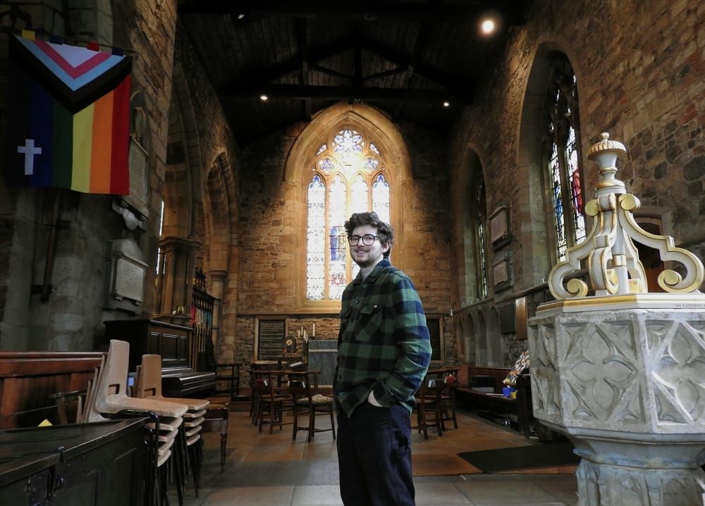 Jay in black work trousers and a green and black plaid top stands near the front at St Nicks.