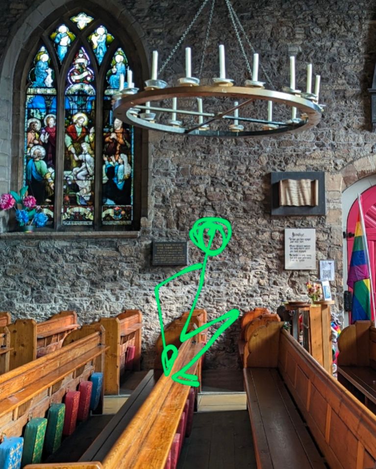 A photo of the pews at St nicks with a green stickman drawn perched on the edge of the pew.