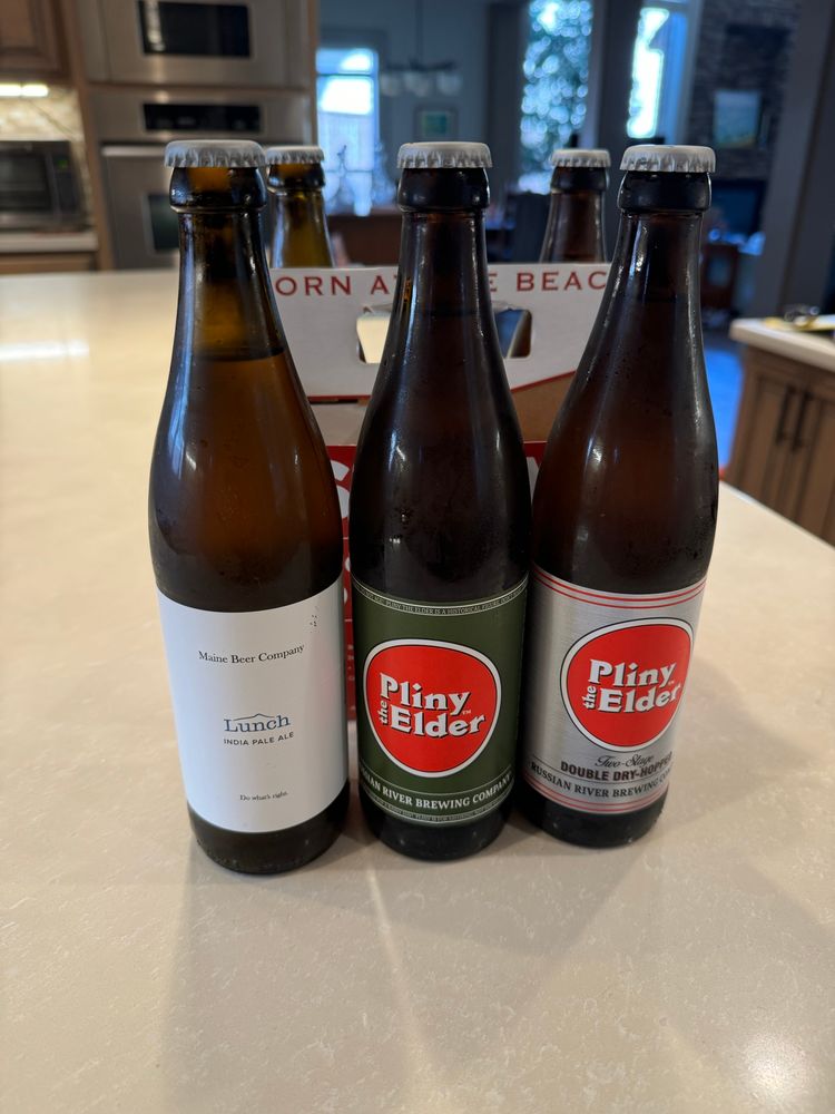 Bomber bottles of Maine Beer Company’s Lunch IPA, Russian River’s Pliny the Eder, and Russian River’s Pliny the Elder DDH on a kitchen countertop.