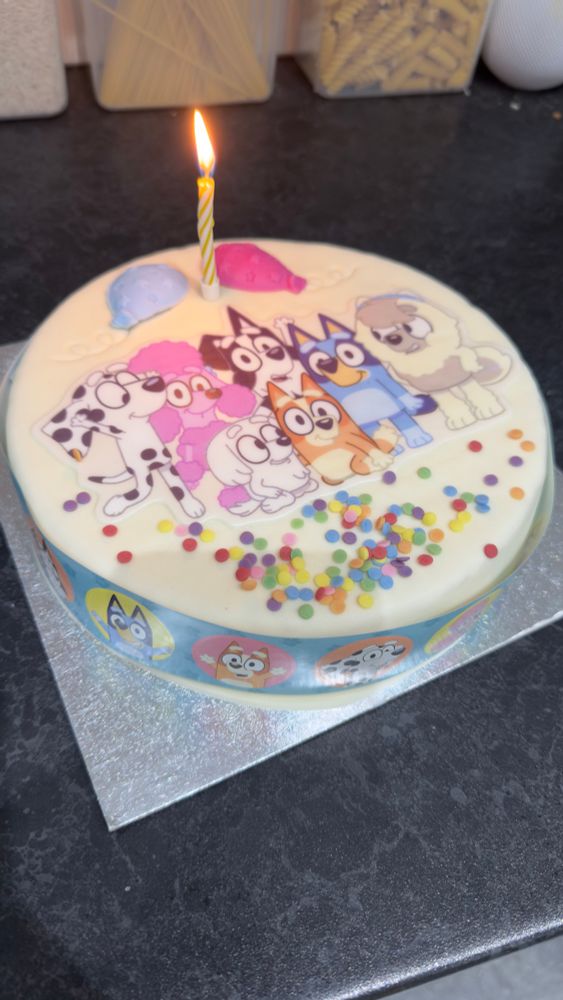An image of a Bluey birthday cake with a single candle lit on top.