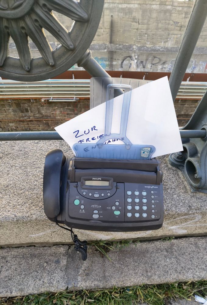 Abgestelltes Telefon- und Faxgerät neben einem Gehweg mit Zettel "Zur freien Entnahme"