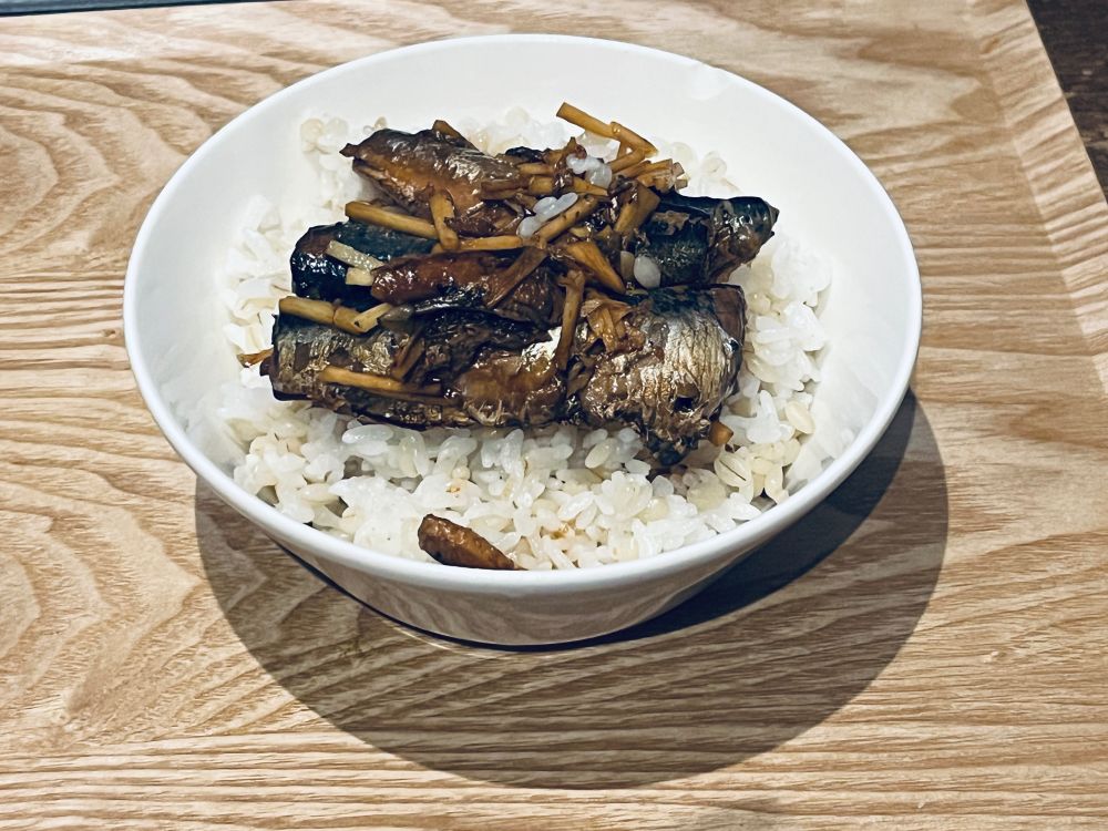 白いスープのお椀に盛られた麦ご飯と醤油で味付けしたオイルサーディンの写真。