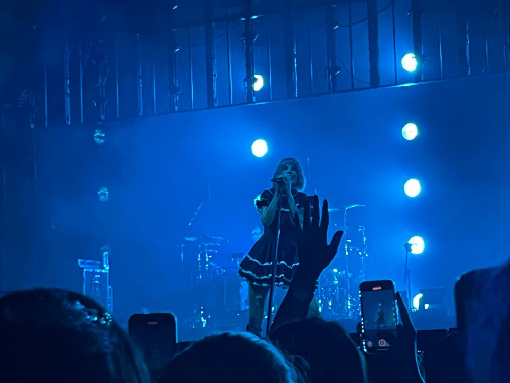 Halsey singing in concert, their hair and stage lights are blue, black dress.