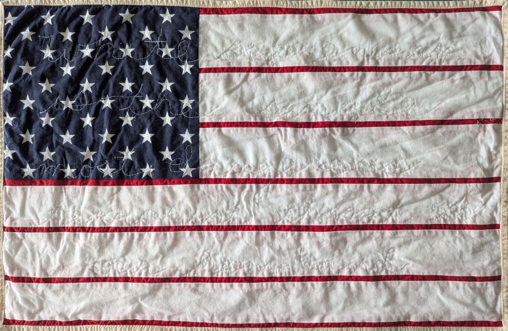 Protest quilt: American flag with oversized white stripes. White thread quilted into the surface reads: "white supremacy is the single most dangerous terrorist threat to our homeland" 