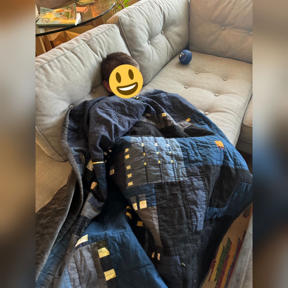 Child wrapped in cityscape quilt. Smiling under the emoji sticker. 