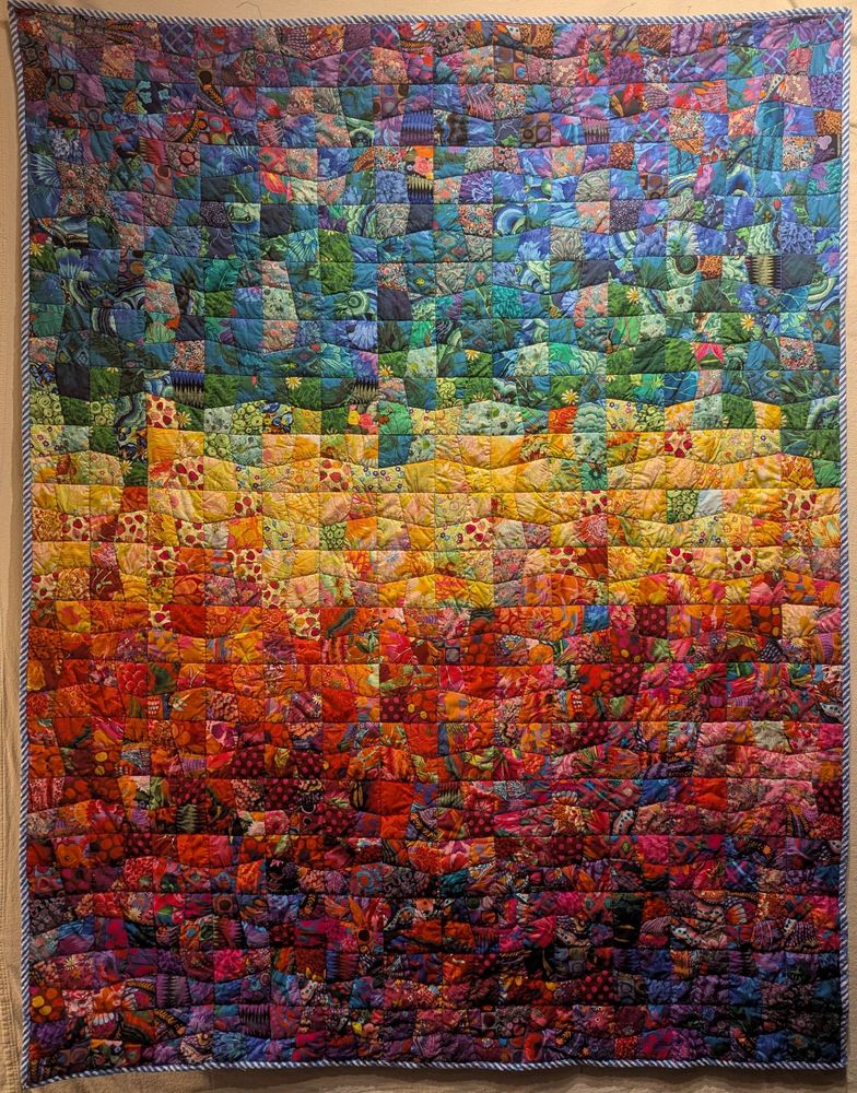 A finished quilt made with rainbow fabrics in a wonky four-patch pattern, trimmed with blue and white stripe bias tape