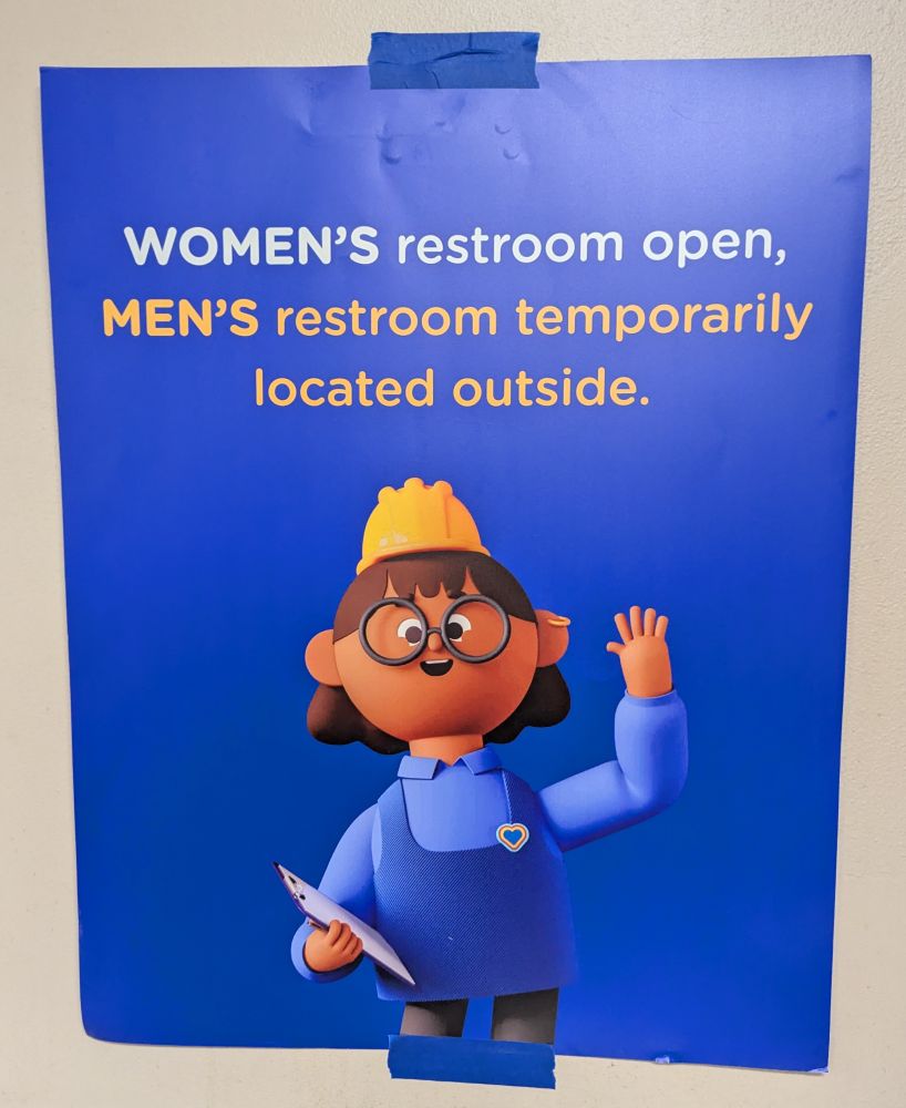 A sign featuring a smiling cartoon construction worker waving with the caption "WOMEN'D restroom open, MEN'S restroom temporarily located outside "