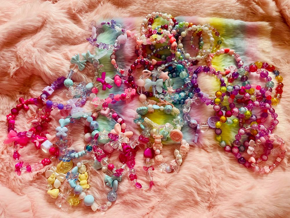 Pink furry background covered in a lot of cute beaded bracelets in pastels and bright colors 
